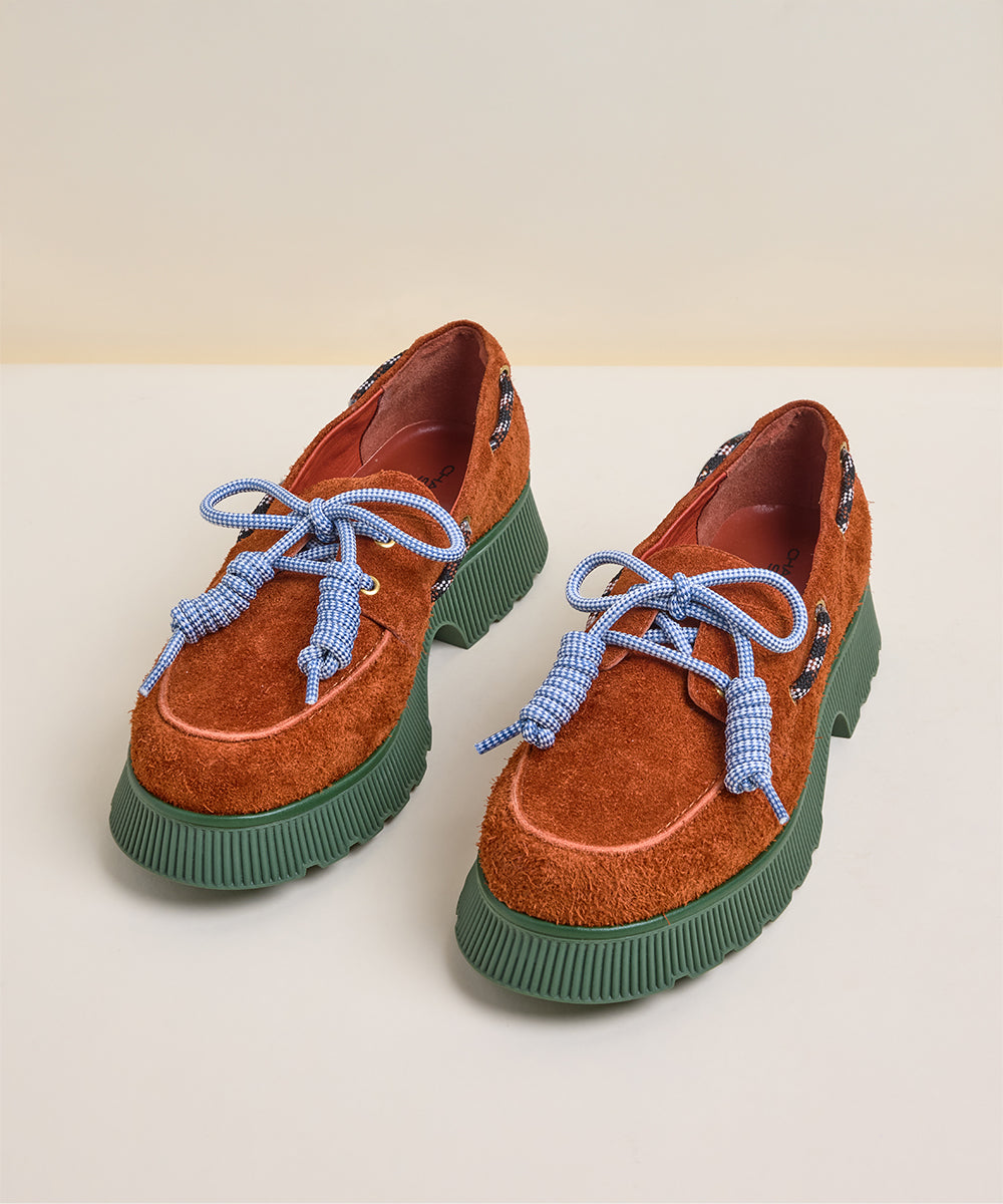 Front view of brown suede loafers with blue laces on a light beige background by Charlotte Stone