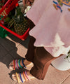Person wearing colorful mismatch suede sandals with a pineapple in a red basket on a tiled floor.