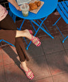 Person sitting at a blue table with food and a drink, wearing pink striped leather sandals.