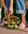 Person wearing multi-color green and pink sandals holding a basket of limes.