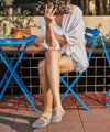 Person sitting at a table with a drink and food, wearing a white shirt and striped canvas slip-on backless shoes.